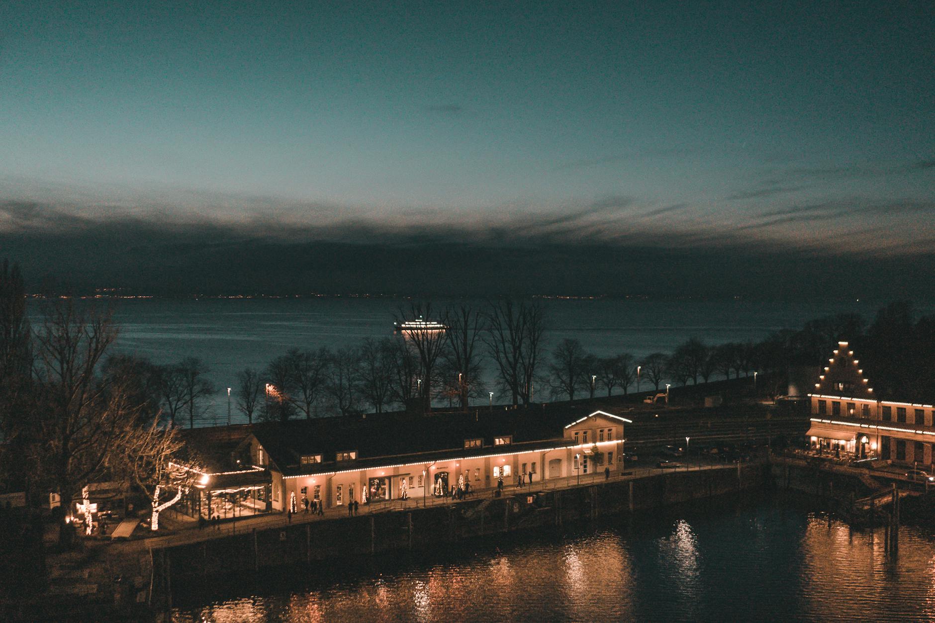 Twilight at Lindau's lakeshore with illuminated buildings and trees lined by Lake Constance.