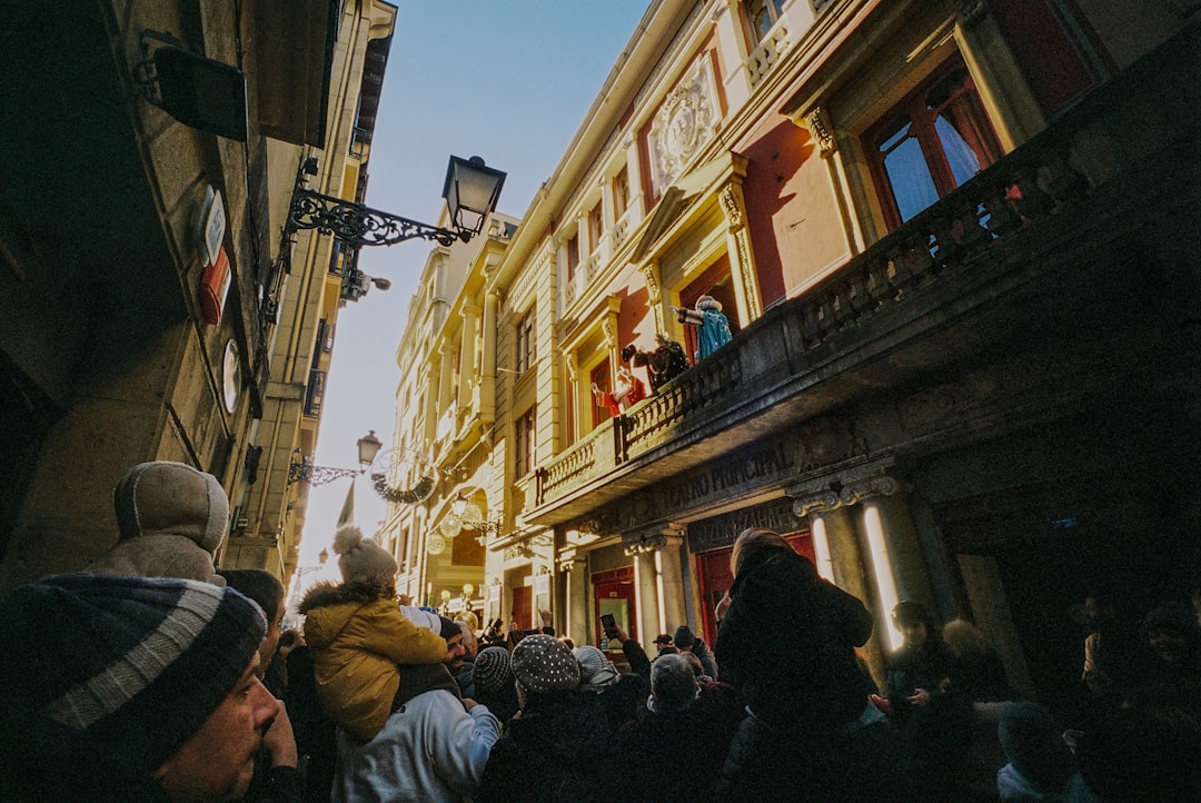 People gathered on a street watching a balcony event.