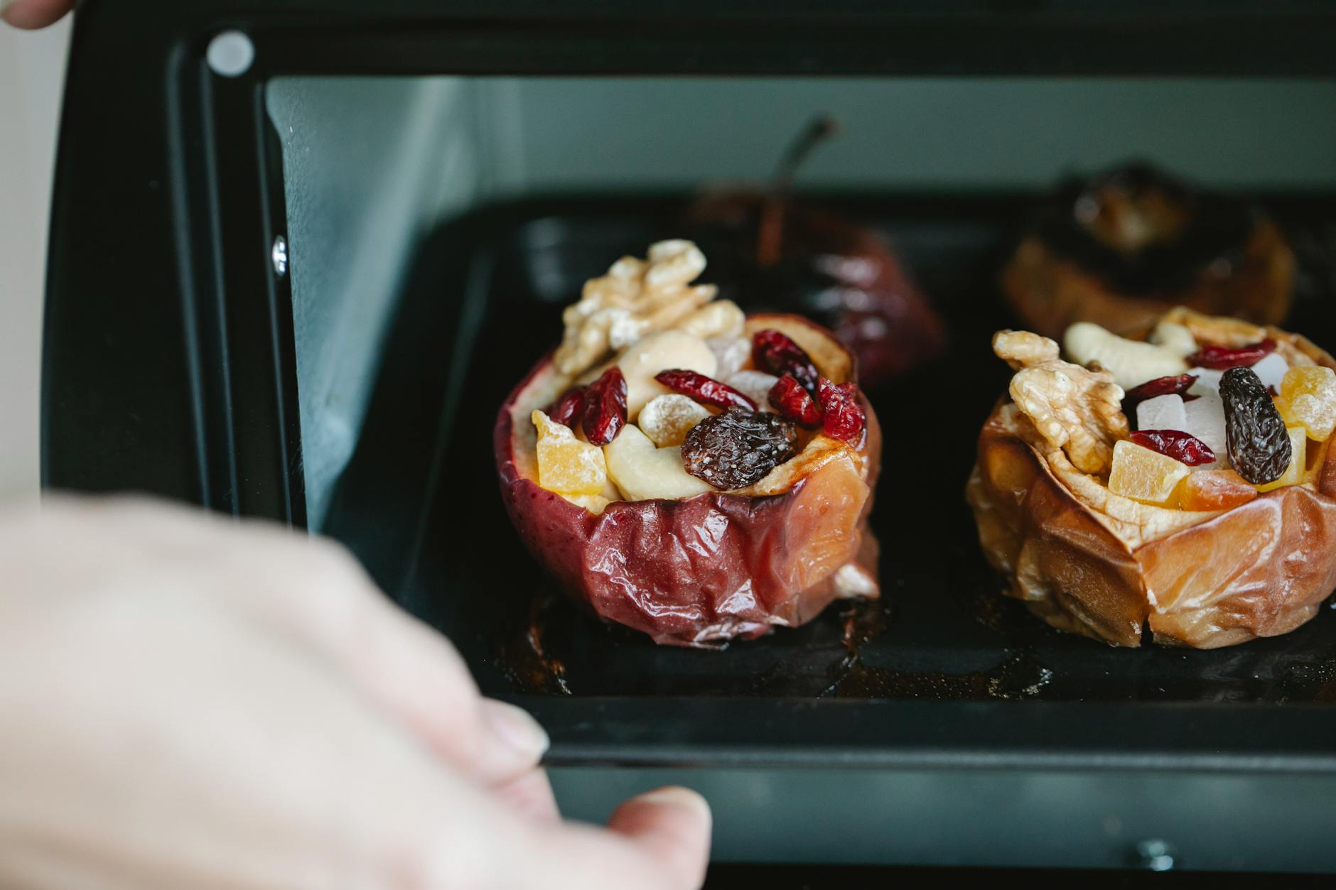 Crop unrecognizable chef removing baking sheet with appetizing stuffed baked apples from electric oven at home